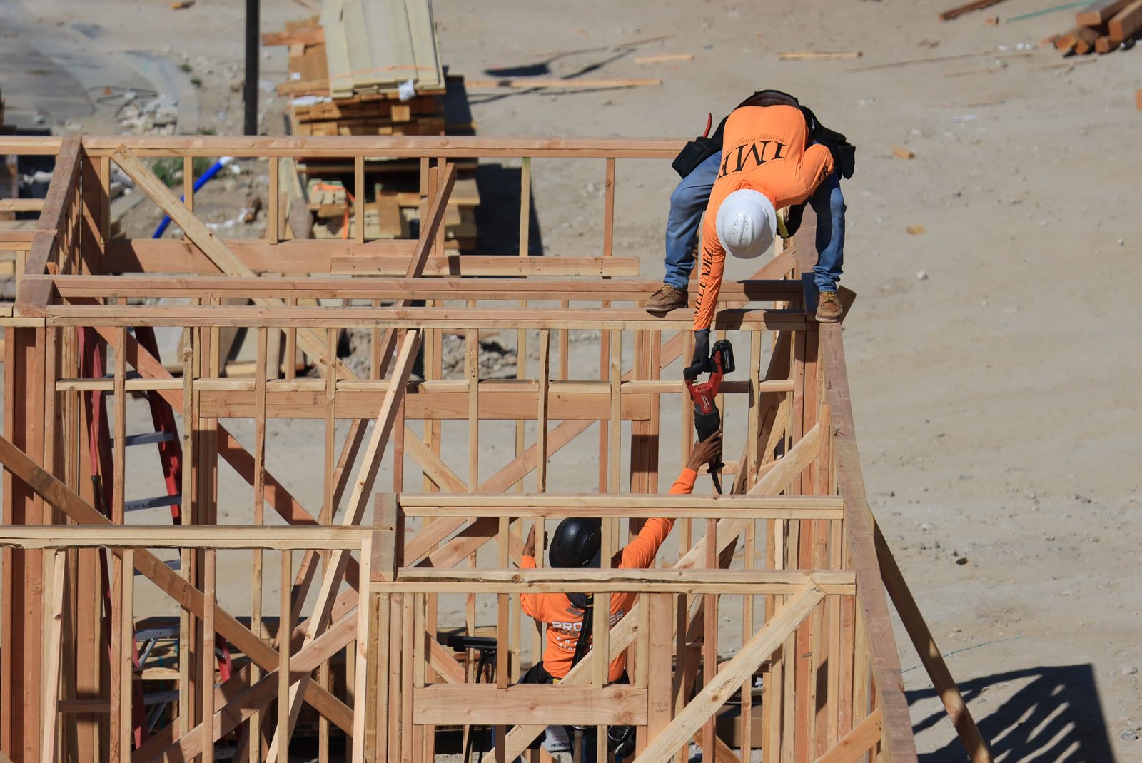 Overhead view of two framing crew members in orange hi-vis and hard hats working on a wood-framed wall